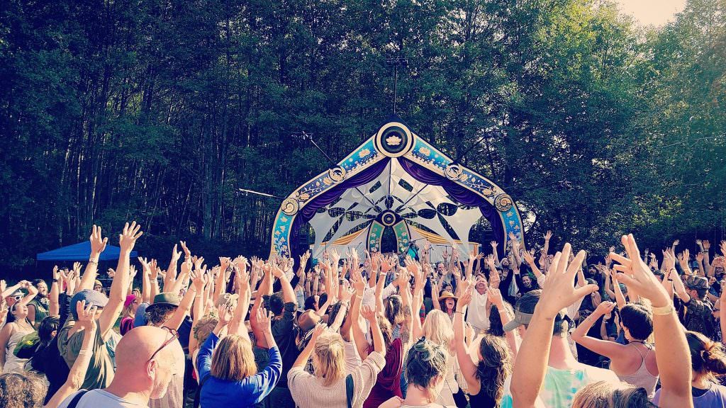 What’s all this Spirituality stuff about, and can I do it too …? 10 Festival crowd raising their hands toward a decorated woodland stage.