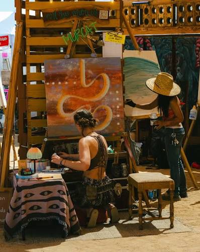Artists working in a shaded outdoor festival vendor space