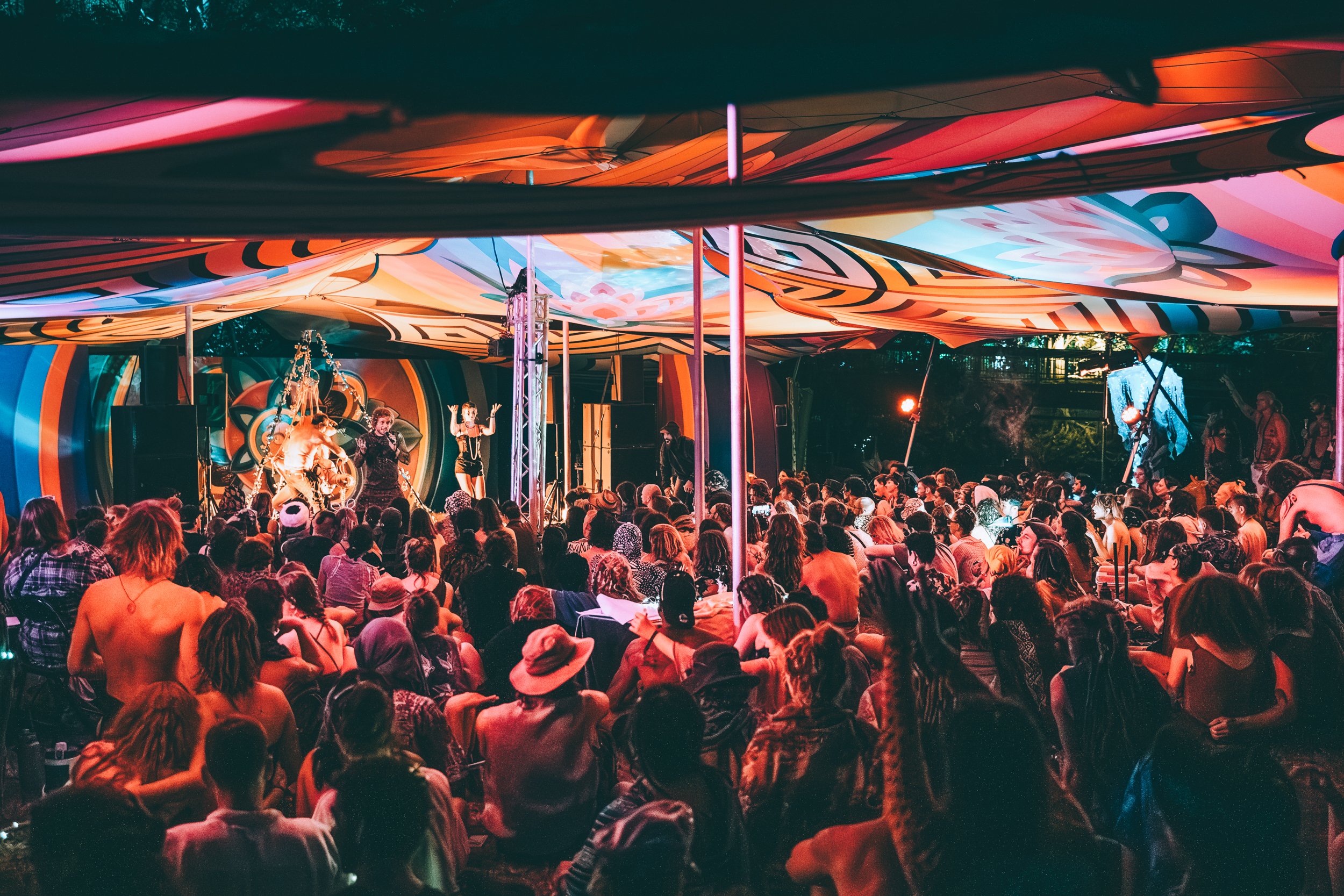 A seated festival audience watching a colourful live performance in Frequency Village.