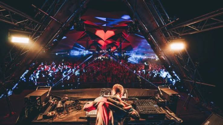 DJ performs to a nighttime crowd beneath geometric stage lighting