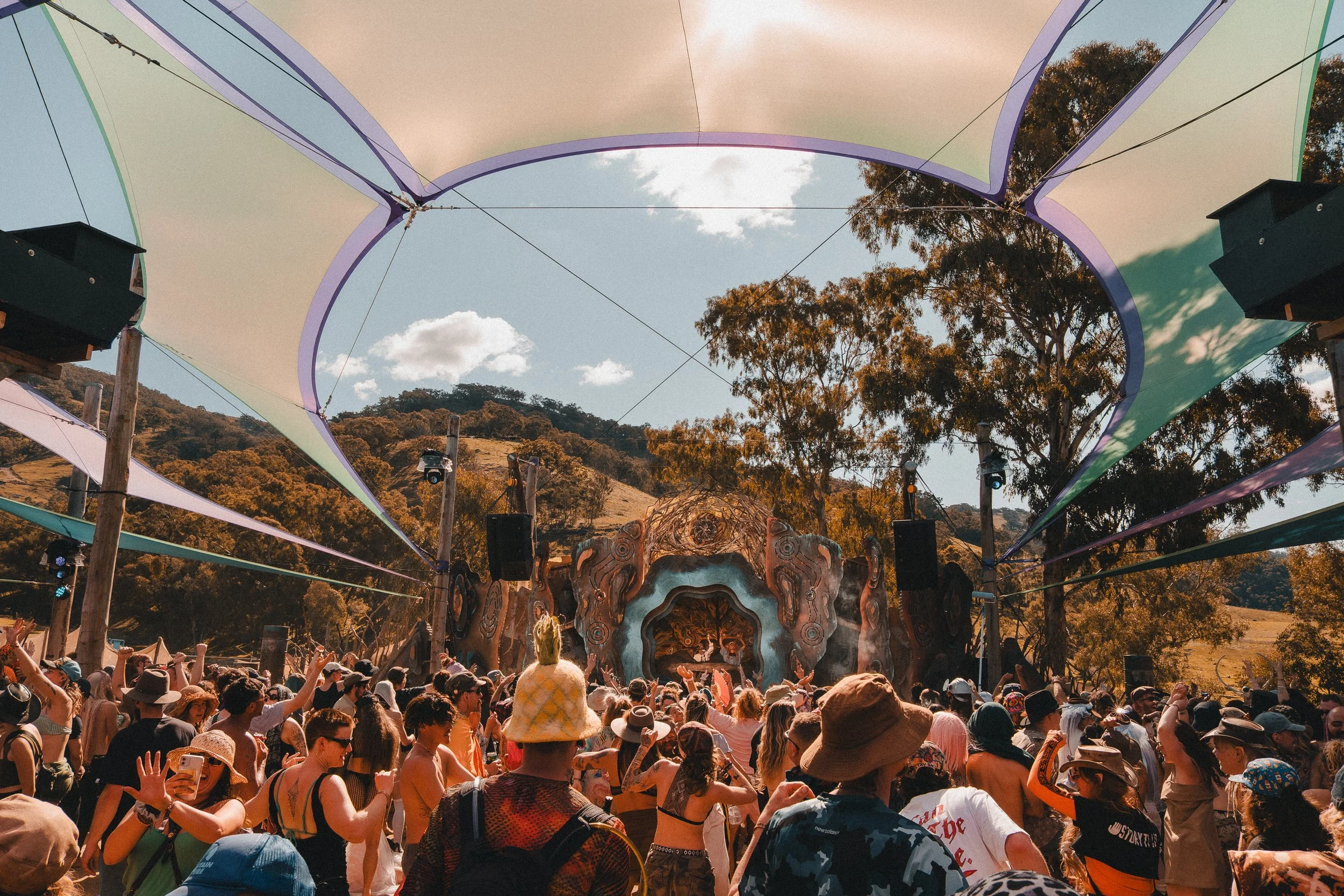 Daytime crowd faces a sculptural stage beneath shade sails