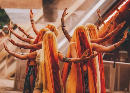 Performers in orange veils pose with raised arms