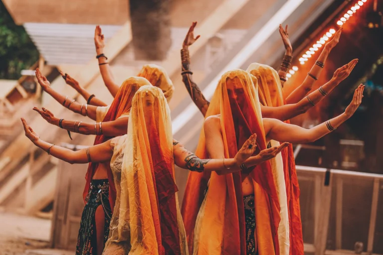 Performers in orange veils pose with raised arms