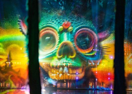 Colourful skull-shaped projections appear across mist screens over Spirit Lake at night.