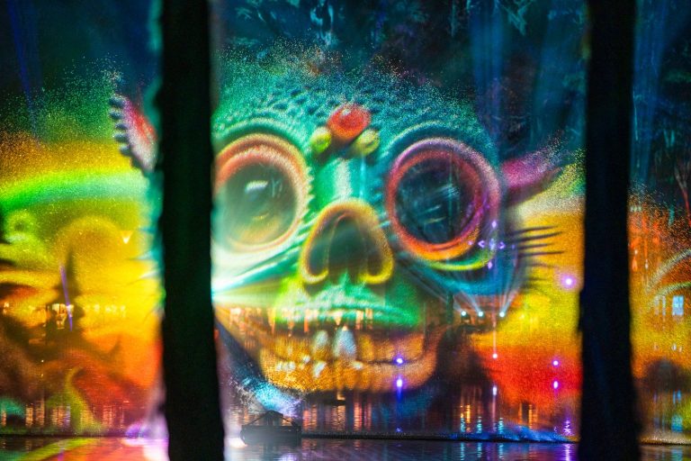 Colourful skull-shaped projections appear across mist screens over Spirit Lake at night.